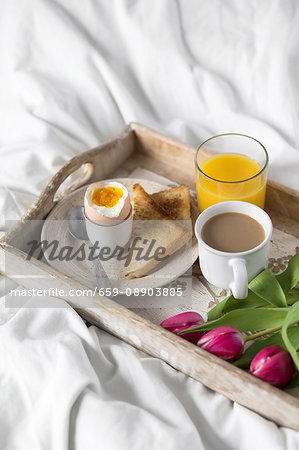 A breakfast tray in bed with a soft-boiled egg, toast, coffee and orange juice for Mother's Day