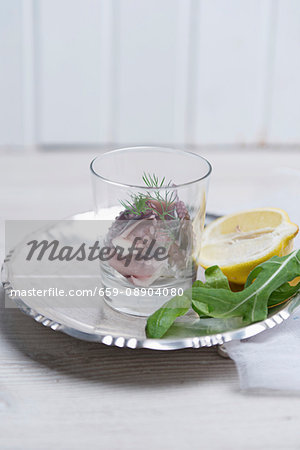 Squid with fresh dill in a glass on a metal plate with a rocket leaf and half a lemon