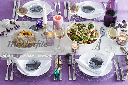 Table laid for Christmas in purple with various dishes, glasses of white wine and animal place setting decorations