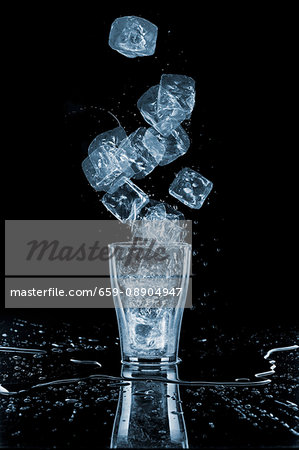 Glass of water with ice cubes around, close-up