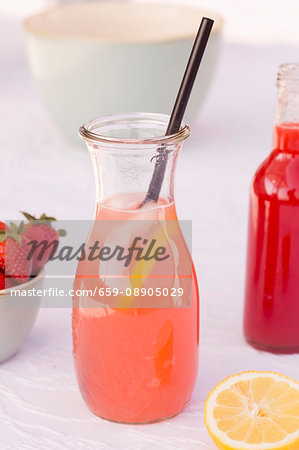 A carafe of homemade rhubarb and strawberry lemonade with lemons