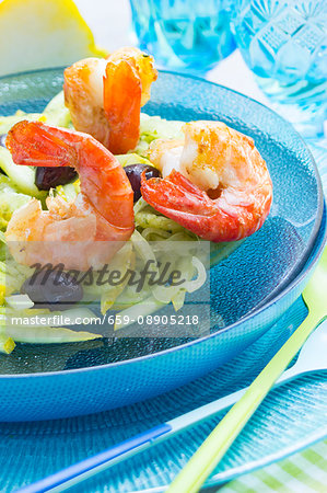 King prawns on a lemon and fennel salad with black olives on a glass turquoise plate