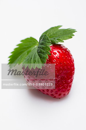 A strawberry with a leaf on a white surface A strawberry with a leaf on a white surface
