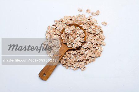 A pile of spelt flakes with a wooden spoon on a white surface