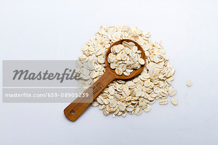 A pile of barley flakes with a wooden spoon on a white surface