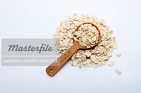 A pile of oats with a wooden spoon on a white surface