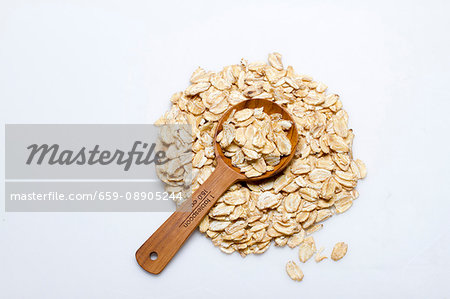 A pile of kamut flakes with a wooden spoon on a white surface A pile of kamut flakes with a wooden spoon on a white surface