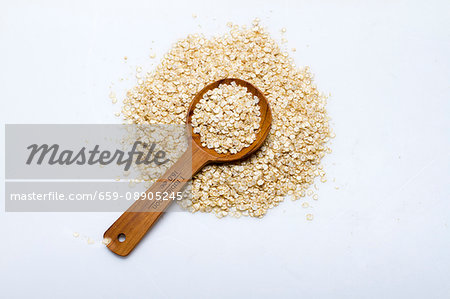 A pile of quinoa flakes with a wooden spoon on a white surface A pile of quinoa flakes with a wooden spoon on a white surface