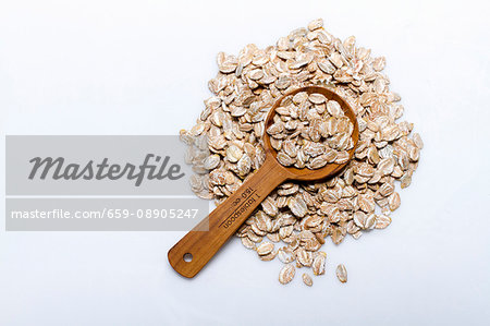 A pile of rye flakes with a wooden spoon on a white surface A pile of rye flakes with a wooden spoon on a white surface