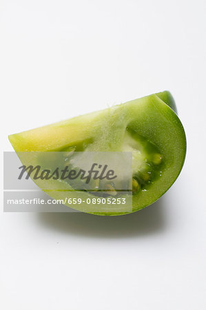 A wedge of green tomato on a white surface