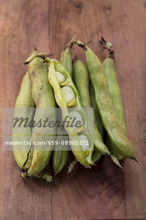 Broad beans in pods on a wooden surface