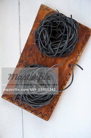Two pasta nests made of black sepia pasta on a wooden board Two pasta nests made of black sepia pasta on a wooden board