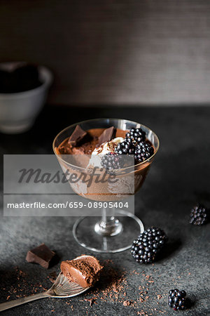 A stem glass with dark chocolate mousse, blackberries and chocolate chunks against a dark background