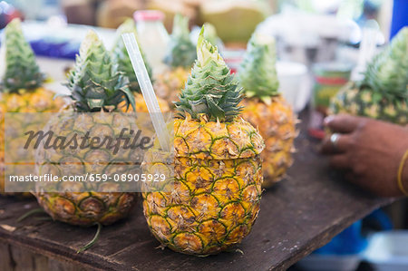 Pineapples with their tops sliced off with straws at a market