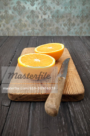 An orange cut in half with a knife on a wooden chopping board