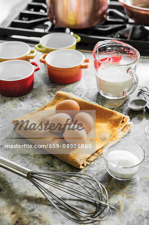 Eggs, milk and sugar with a whisk and ramekins next to a gas stove