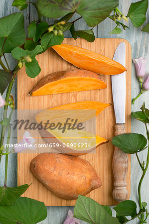 A sliced sweet potato with sweet potato leaves and flowers