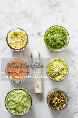 Assorted jars of pesto on a marble surface with a pestle