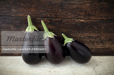Three aubergines in front of a wooden wall