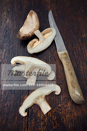 A sliced shiitake mushroom with a knife on a wooden surface