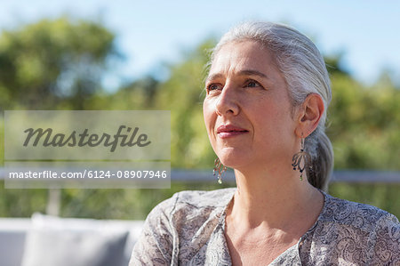 Portrait pensive, serious mature woman looking away on sunny patio