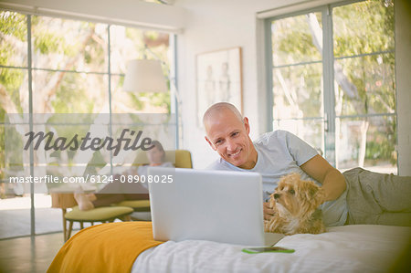 Smiling man with dog using laptop on bed