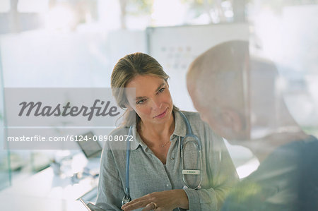 Serious female doctor with digital tablet talking to male patient in doctor’s office