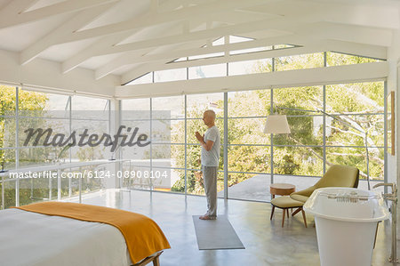 Mature man practicing yoga with hands at heart center in modern bedroom with vaulted wood beam ceilings