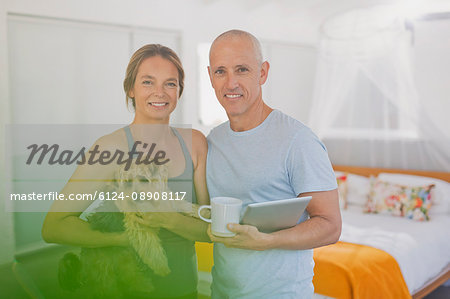 Portrait smiling mature couple with dog and digital tablet in bedroom