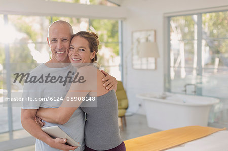Portrait happy mature couple with digital tablet hugging in bedroom