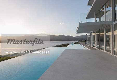 Sunny, tranquil modern luxury home showcase exterior with infinity pool and sunset ocean view