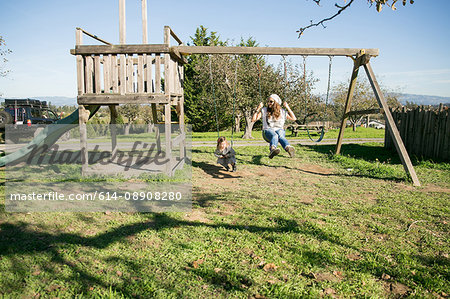 Mid adult woman and daughter sitting on swings in park