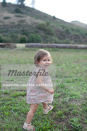 Cute female toddler running in field looking over her shoulder