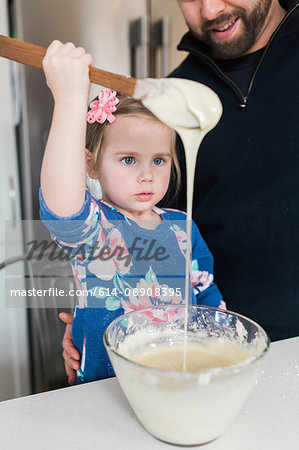 Girl with father gazing at wooden spoon drizzle at kitchen counter
