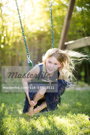Portrait of girl crouching while swinging on garden swing