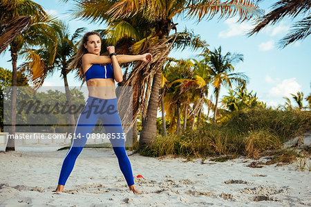 Young woman training, crossing and stretching arms at beach