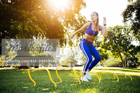 Young woman training between agility hurdles in park