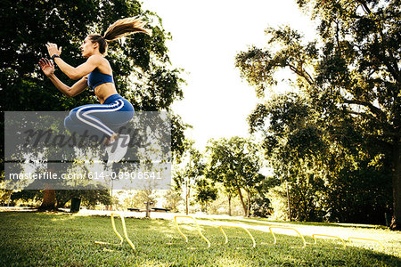Young woman training, jumping between agility hurdles in park