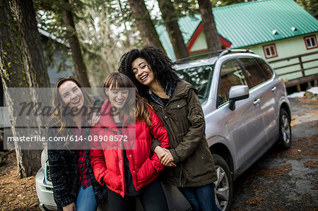 Portrait of three friends standing beside car, laughing