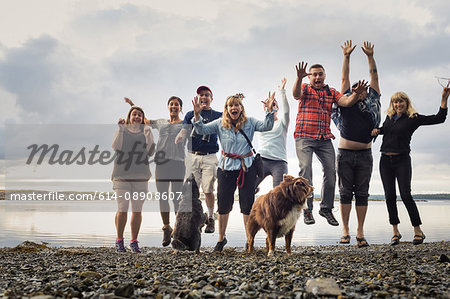 Portrait of adult family with dogs jumping on shingle beach, Maine, USA
