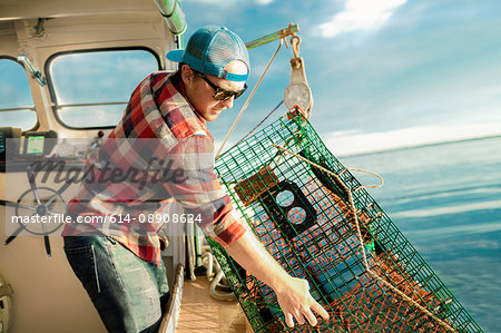 Young man lifting lobster cage from winch on fishing boat on coast of Maine, USA