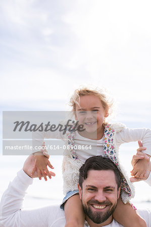 Portrait of mature man giving daughter a shoulder carry at coast