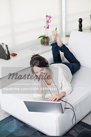 Beautiful brunette woman on a couch with computer and headphones