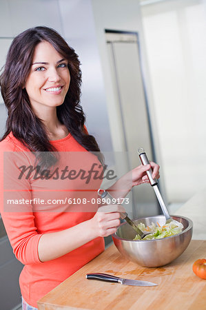 Pretty brunette woman preparing a salad in the kitchen smiling at camera