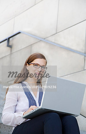 Pretty businesswoman with laptop sitting at the stairs of a building in her break