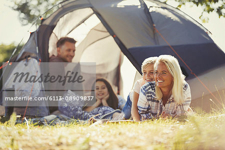 Smiling family relaxing outside sunny tent at campsite