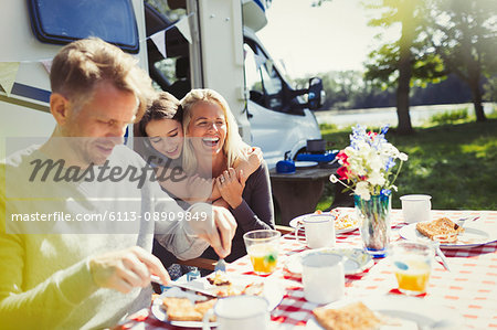 Happy family hugging and eating breakfast outside sunny motor home