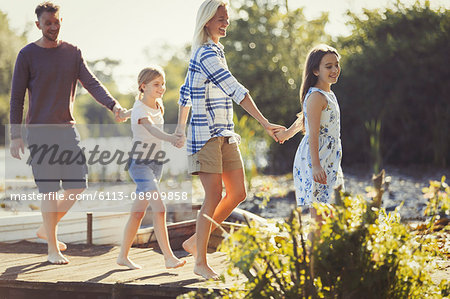 Barefoot family holding hands and walking on dock