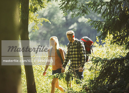 Couple with backpacks hiking in sunny woods