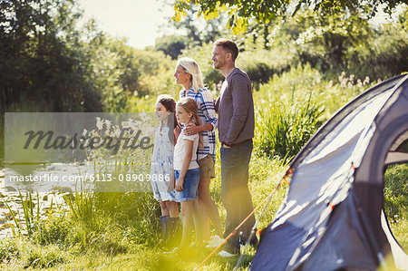 Family at sunny campsite lakeside looking away
